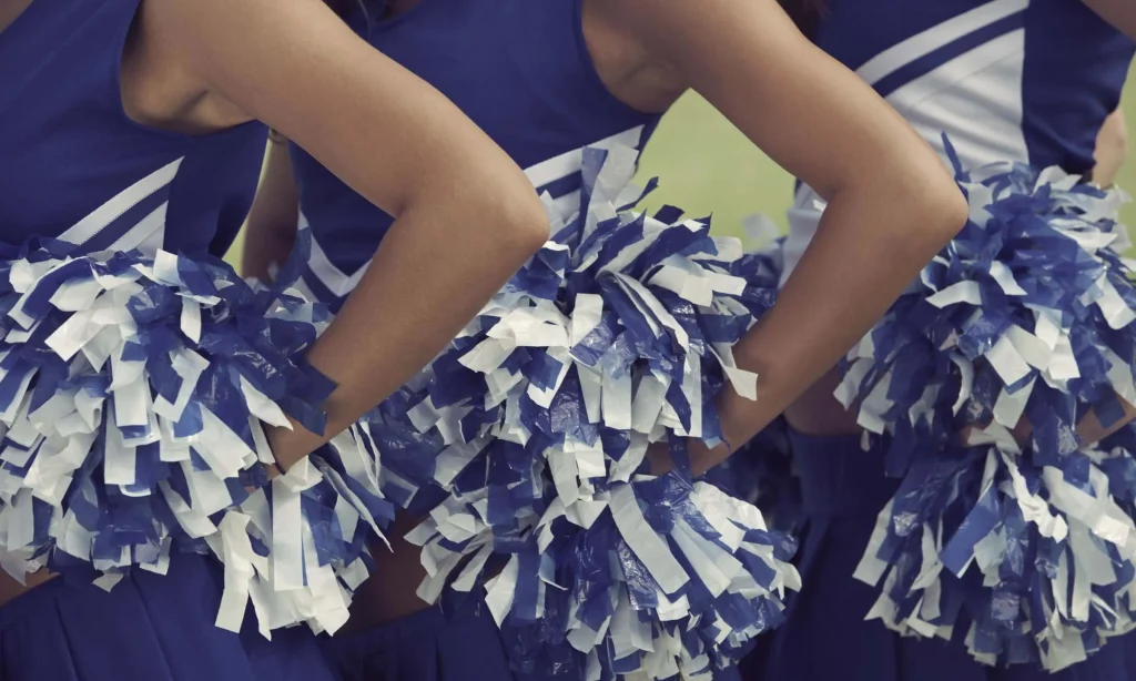 Close up of 3 cheerleaders wearing blue uninforms and holding blue and white pom poms.