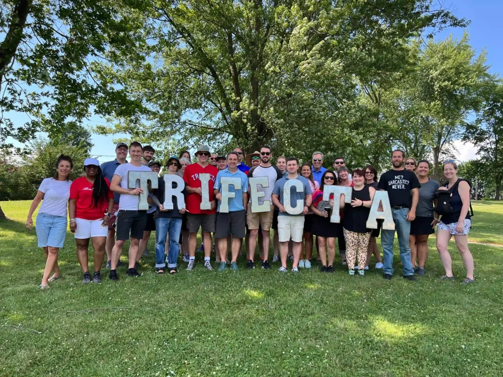 A group of Trifecta employees outside holding up a Trifecta sign.